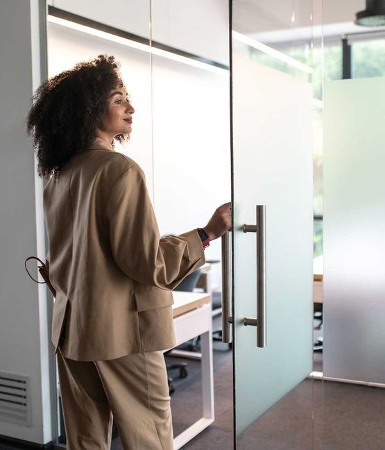 Selbstbewusste und entschlossene Geschäftsfrau betritt ein modernes Büro mit Glastüren