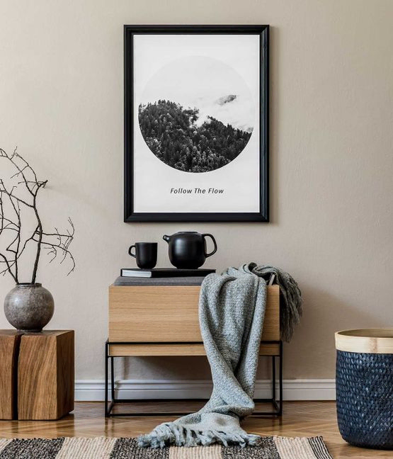 Moderne skandinavische Wohnzimmereinrichtung mit schwarzem Posterrahmen, Design-Kommode, Blatt in Vase, schwarzem Rattankorb, Büchern und eleganten Accessoires.